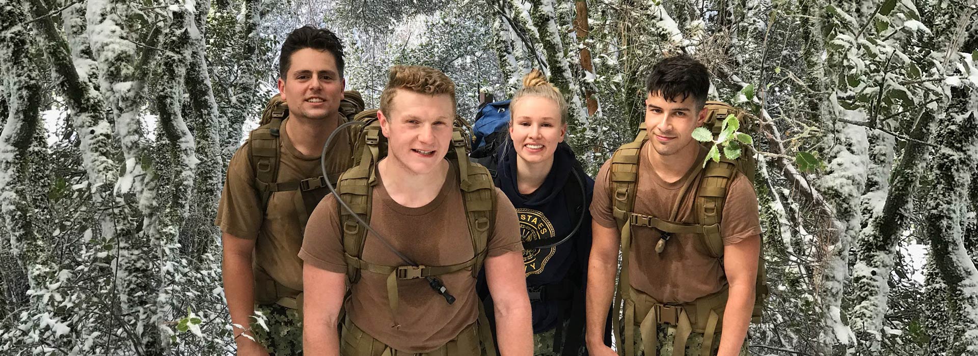 Group of four midshipmen hiking with backpacks in a forest filled with snow