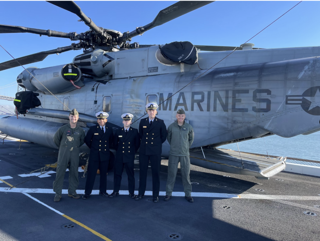 Five military personnel in uniform in front of a Marines Helicopter