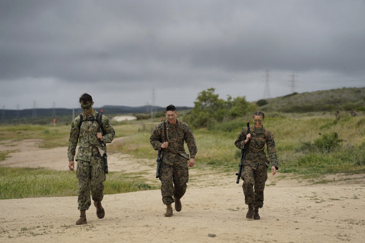 Group of three midshipmen dressed in camouflage uniform on a cloudy field
