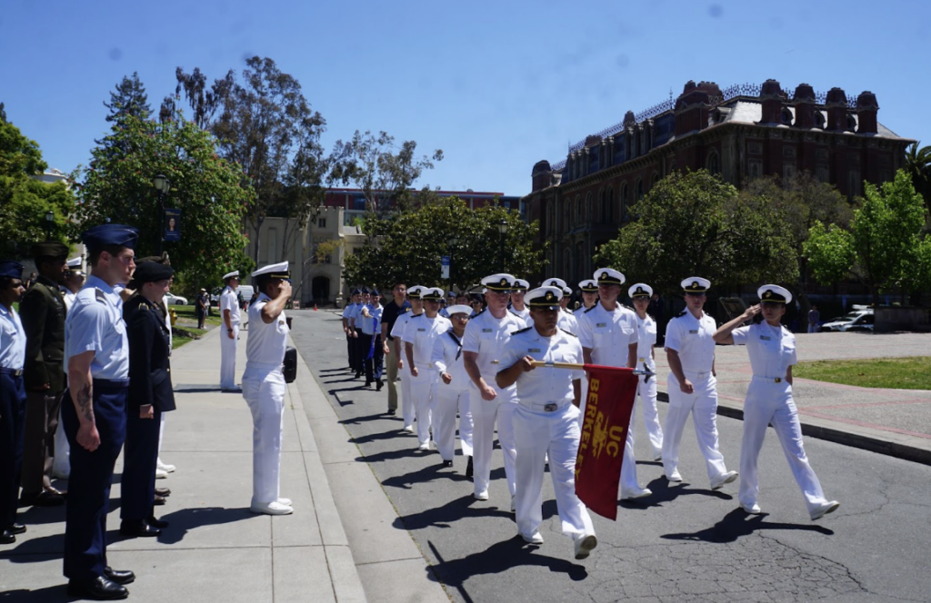 Large group of midshipmen dressed in summer whites uniform marching on campus for the Tri-Service parade